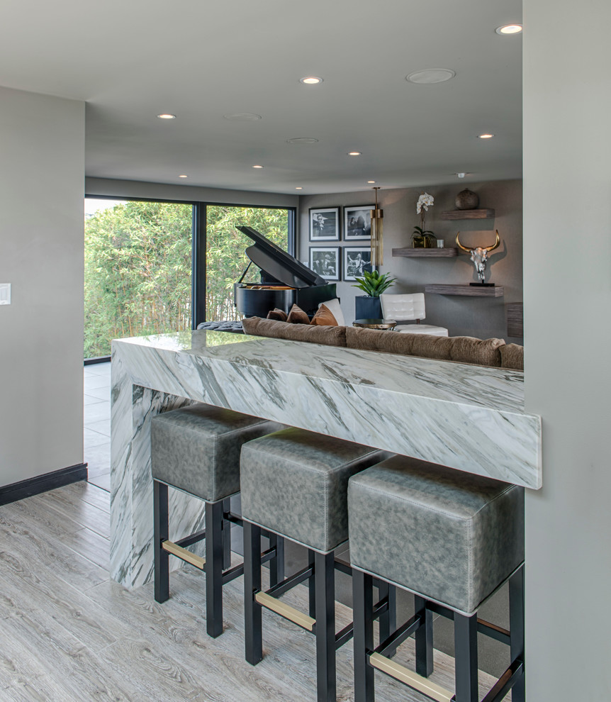 Eat-in kitchen - large contemporary l-shaped light wood floor and beige floor eat-in kitchen idea in Los Angeles with a farmhouse sink, recessed-panel cabinets, gray cabinets, marble countertops, gray backsplash, stone slab backsplash, white appliances and an island