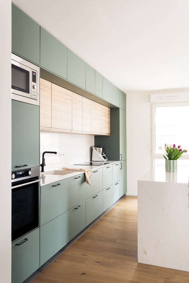 Photo of a mid-sized scandinavian single-wall open plan kitchen in Paris with an integrated sink, beaded inset cabinets, green cabinets, quartzite benchtops, white splashback, engineered quartz splashback, stainless steel appliances, light hardwood floors, with island and white benchtop.