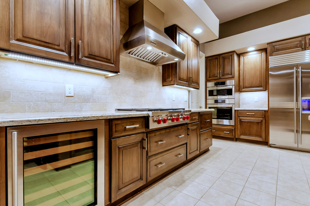 Open concept kitchen - large transitional l-shaped ceramic tile and white floor open concept kitchen idea in Phoenix with an undermount sink, raised-panel cabinets, medium tone wood cabinets, solid surface countertops, white backsplash, stainless steel appliances and an island