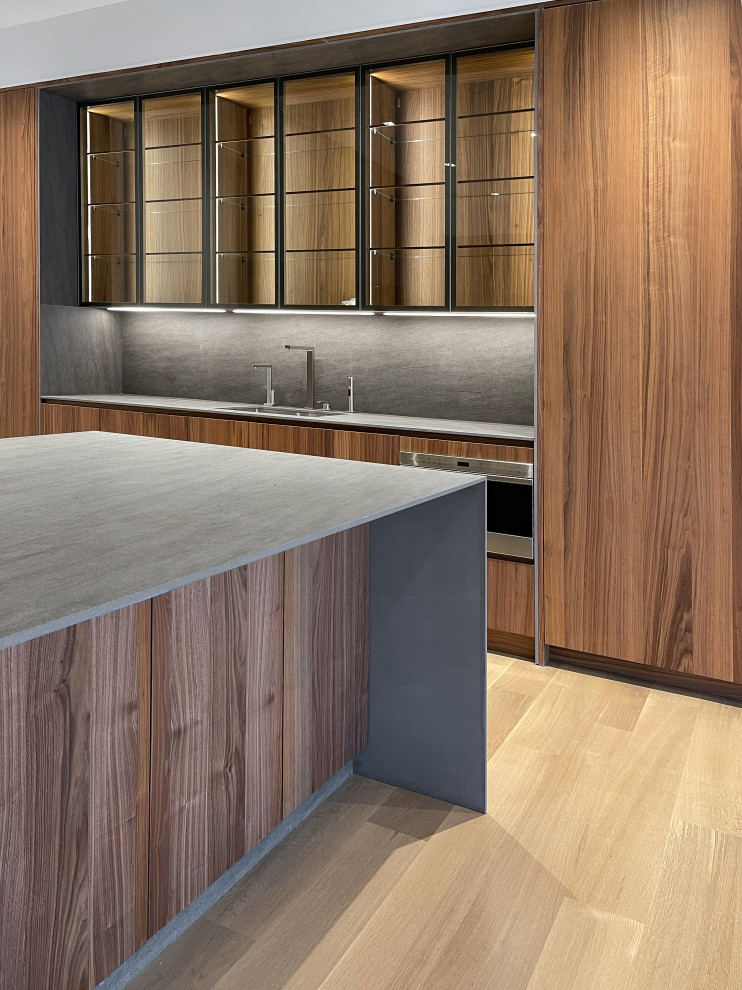 Immagine di un'ampia cucina minimalista con lavello sottopiano, ante lisce, ante in legno scuro, paraspruzzi grigio, elettrodomestici da incasso, parquet chiaro e top grigio