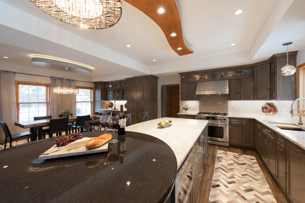 This is an example of a large transitional galley open plan kitchen in Minneapolis with an undermount sink, recessed-panel cabinets, brown cabinets, granite benchtops, grey splashback, porcelain splashback, stainless steel appliances, light hardwood floors, with island, multi-coloured floor and multi-coloured benchtop.