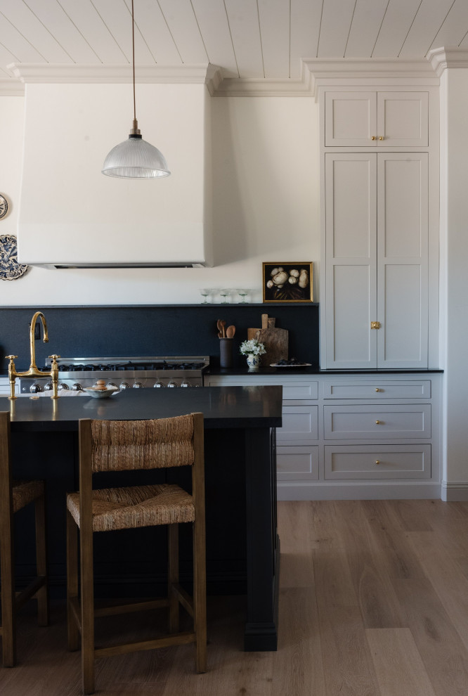 Design ideas for a classic kitchen in Other with a belfast sink, shaker cabinets, white cabinets, granite worktops, black splashback, granite splashback, an island and black worktops.