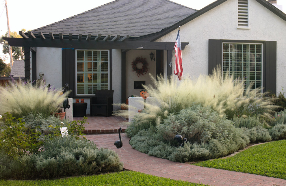 Small mediterranean front yard partial sun xeriscape in Los Angeles with with flowerbed and brick pavers for fall.