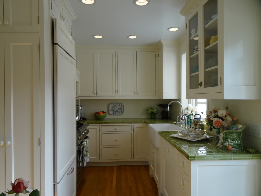 Inspiration for a small country u-shaped eat-in kitchen in Los Angeles with a farmhouse sink, flat-panel cabinets, white cabinets, tile benchtops, green splashback, ceramic splashback, stainless steel appliances, light hardwood floors and no island.