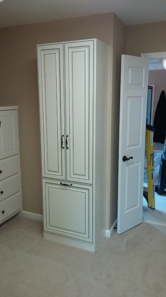 This is an example of a mid-sized traditional gender-neutral walk-in wardrobe in Atlanta with raised-panel cabinets, distressed cabinets, carpet and beige floor.