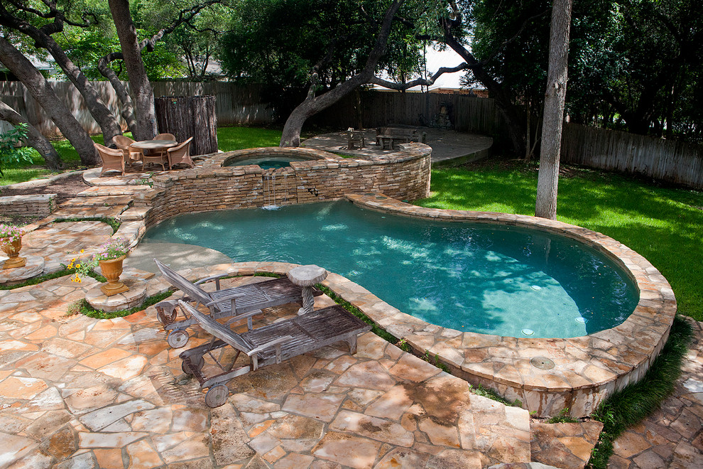Design ideas for a large traditional backyard custom-shaped natural pool in Austin with natural stone pavers and a hot tub.