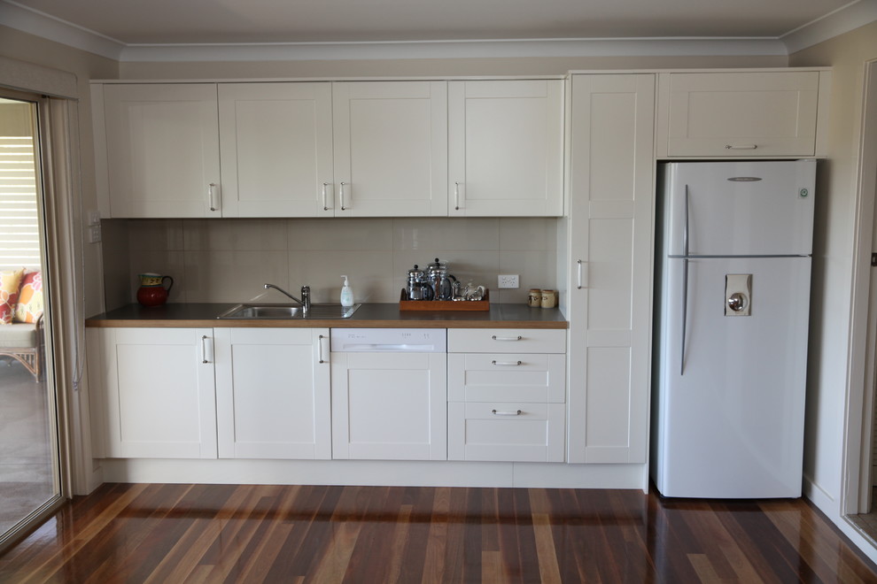 Transitional galley open plan kitchen in Newcastle - Maitland with a double-bowl sink, shaker cabinets, white cabinets, laminate benchtops, white splashback, ceramic splashback, panelled appliances, dark hardwood floors and brown floor.