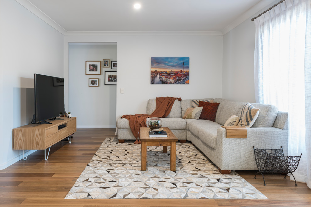 This is an example of a small transitional formal enclosed living room in Brisbane with white walls, medium hardwood floors, a freestanding tv and brown floor.