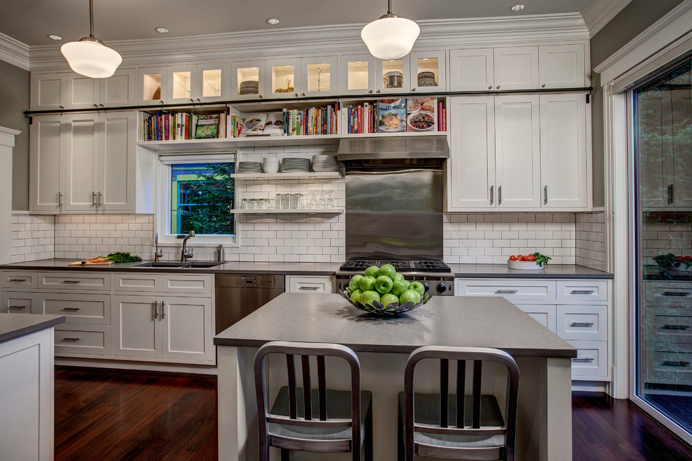 Photo of a transitional kitchen in Seattle with a double-bowl sink, shaker cabinets, white cabinets, white splashback, subway tile splashback, stainless steel appliances and dark hardwood floors.