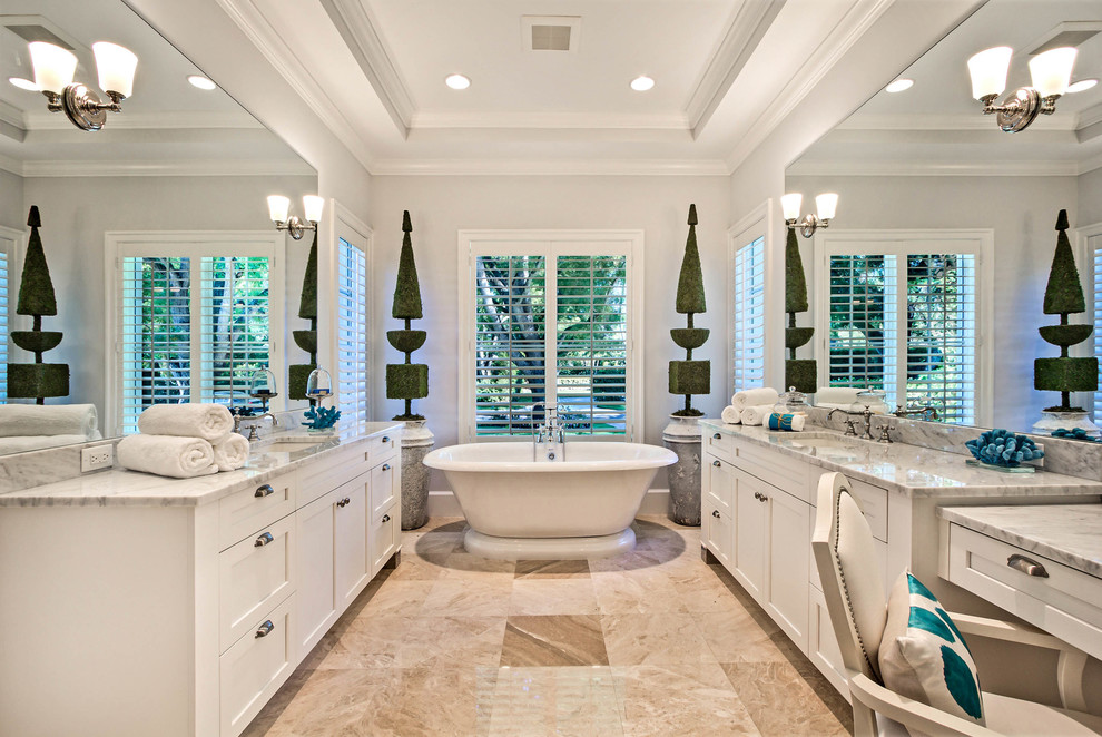 This is an example of a large traditional master bathroom in Miami with shaker cabinets, white cabinets, a freestanding tub, white walls, limestone floors, an undermount sink and beige floor.