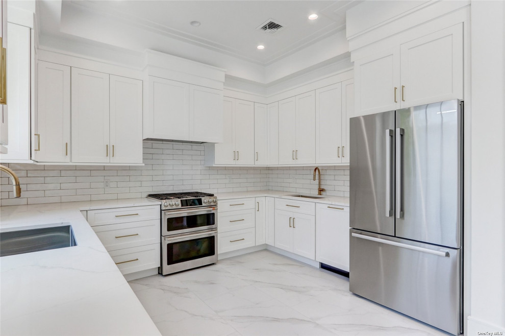 This is an example of a mid-sized traditional u-shaped open plan kitchen in New York with an undermount sink, shaker cabinets, white cabinets, quartz benchtops, white splashback, subway tile splashback, stainless steel appliances, marble floors, no island, white floor and white benchtop.