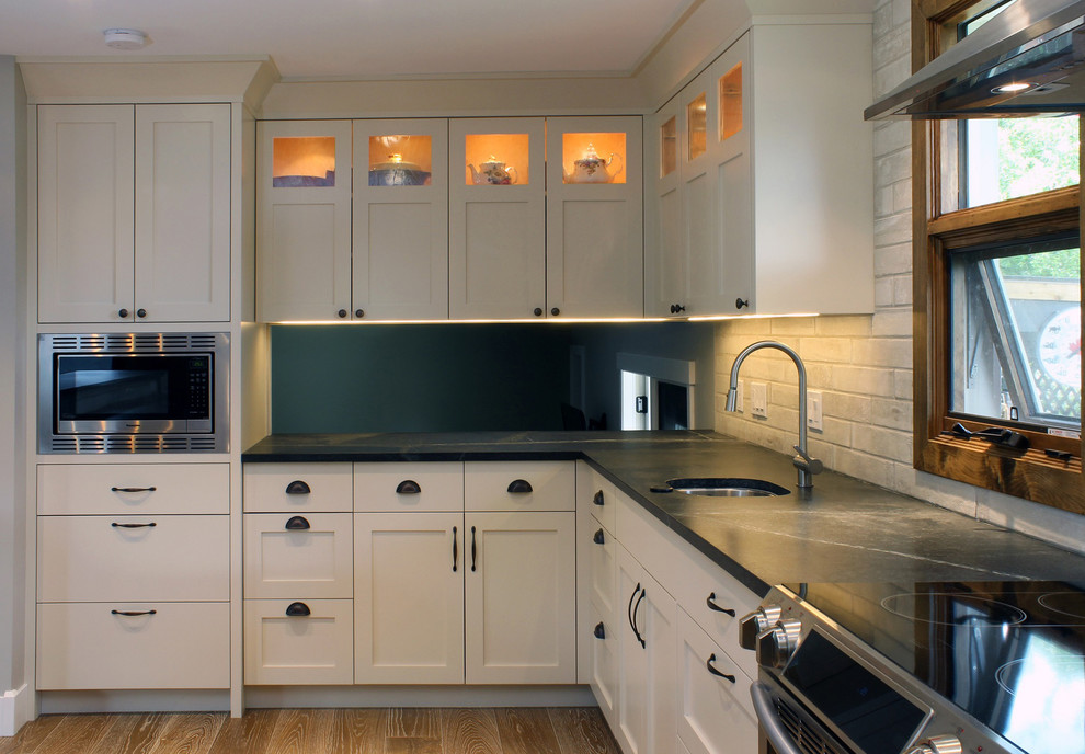 Large transitional u-shaped medium tone wood floor open concept kitchen photo in Calgary with an undermount sink, shaker cabinets, soapstone countertops, ceramic backsplash, stainless steel appliances and an island