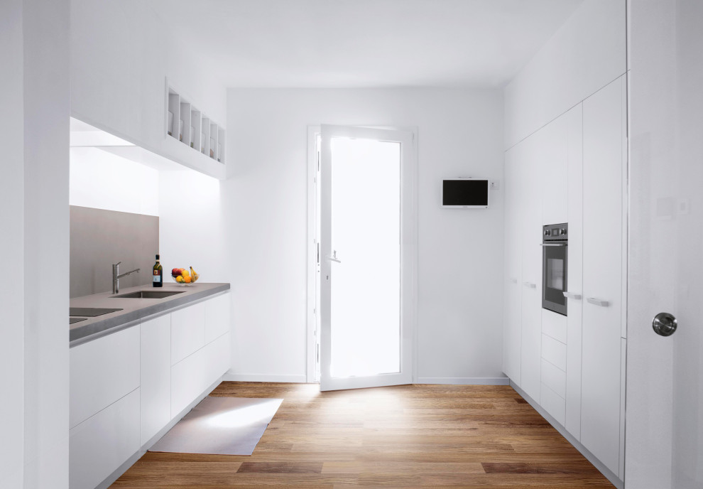 Mid-sized modern galley eat-in kitchen in Florence with an integrated sink, white cabinets, grey splashback, porcelain splashback, stainless steel appliances, dark hardwood floors, brown floor and grey benchtop.
