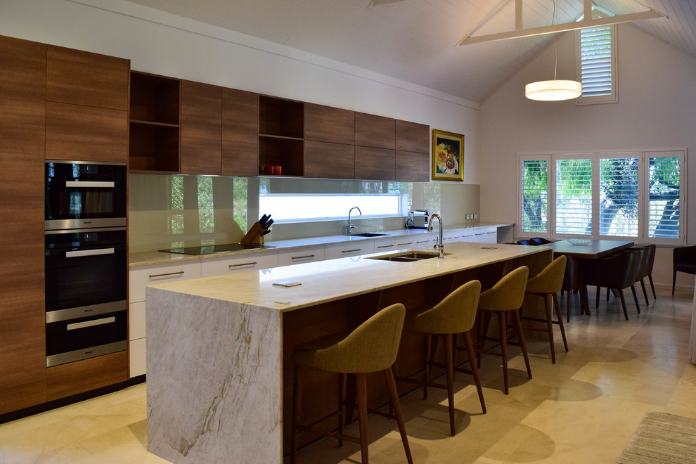 This is an example of a large modern single-wall open plan kitchen in Perth with a drop-in sink, dark wood cabinets, granite benchtops, beige splashback, glass sheet splashback, stainless steel appliances, ceramic floors, with island and beige floor.