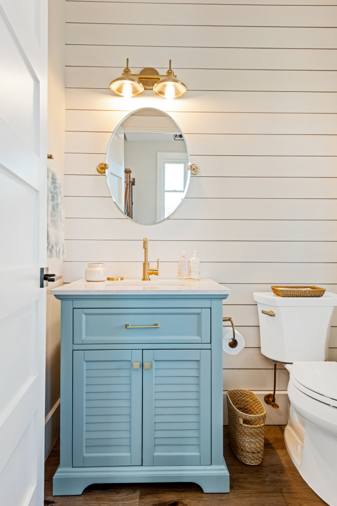 Maritime Gästetoilette mit Lamellenschränken, blauen Schränken, weißer Wandfarbe, braunem Holzboden, Unterbauwaschbecken, braunem Boden, weißer Waschtischplatte, freistehendem Waschtisch und Holzdielenwänden in Charleston