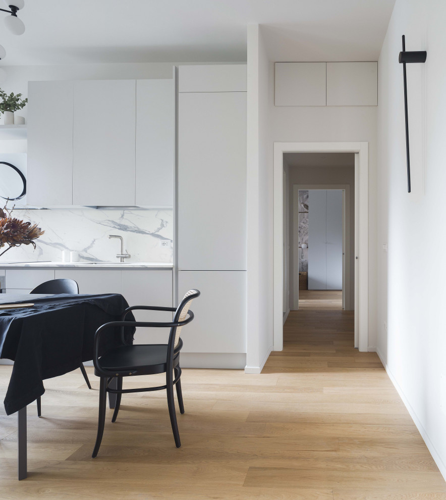 Modern inredning av ett mellanstort vit linjärt vitt kök och matrum, med en undermonterad diskho, släta luckor, beige skåp, vitt stänkskydd, ljust trägolv och beiget golv
