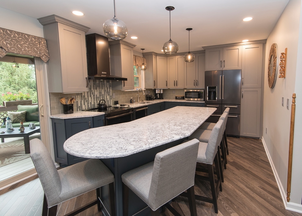Example of a mid-sized transitional l-shaped brown floor eat-in kitchen design in Baltimore with a single-bowl sink, shaker cabinets, gray cabinets, quartz countertops, gray backsplash, subway tile backsplash, stainless steel appliances, an island and white countertops