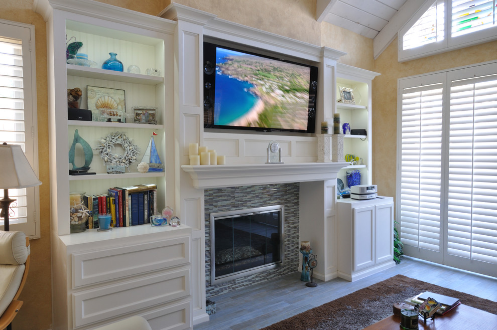 Mid-sized mediterranean living room in Orange County with beige walls, medium hardwood floors, a standard fireplace, a tile fireplace surround and a built-in media wall.