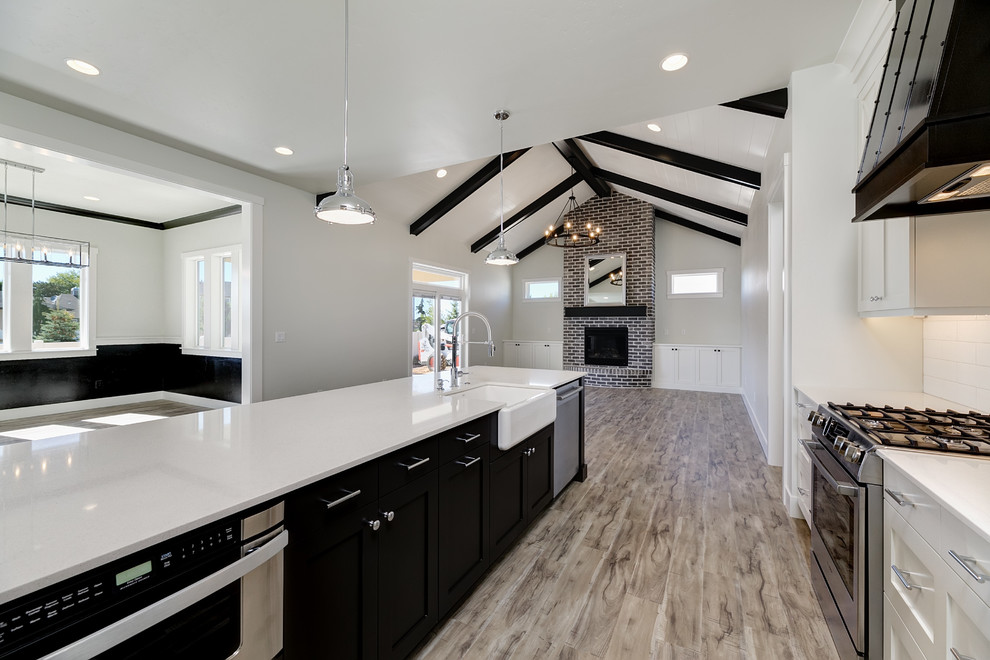 This is an example of a mid-sized country u-shaped eat-in kitchen in Boise with a farmhouse sink, recessed-panel cabinets, white cabinets, quartz benchtops, white splashback, subway tile splashback, stainless steel appliances, vinyl floors, with island, grey floor and white benchtop.