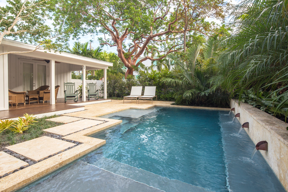 This is an example of a mid-sized beach style backyard pool in Miami with natural stone pavers.