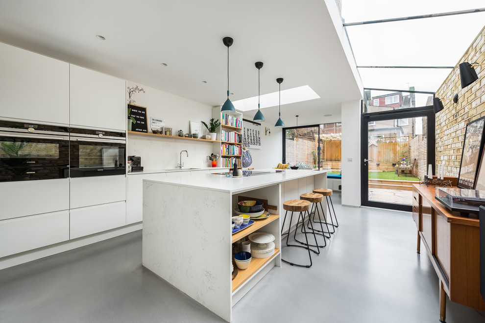 Design ideas for a mid-sized contemporary galley eat-in kitchen in London with flat-panel cabinets, white cabinets, quartzite benchtops, white splashback, concrete floors, with island, grey floor and black appliances.