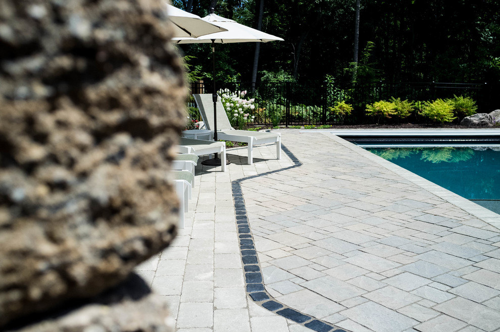 This is an example of a mid-sized traditional backyard rectangular lap pool in Grand Rapids with a water feature and concrete pavers.