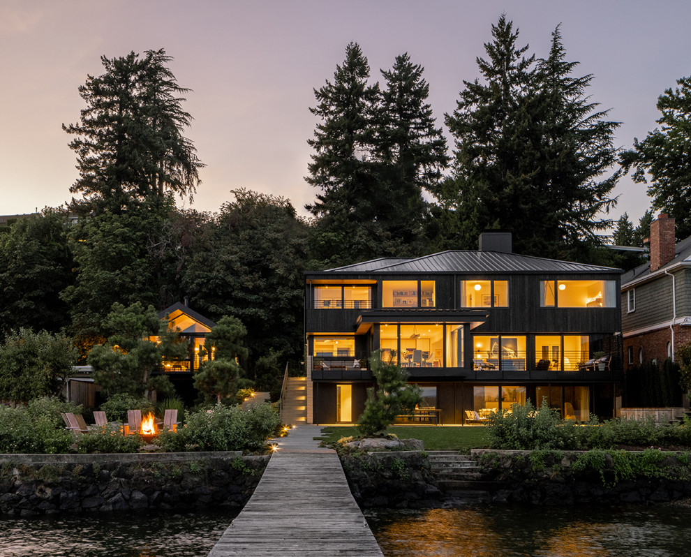 Photo of a black contemporary detached house in Seattle with three floors, wood cladding, a hip roof, a metal roof and a black roof.