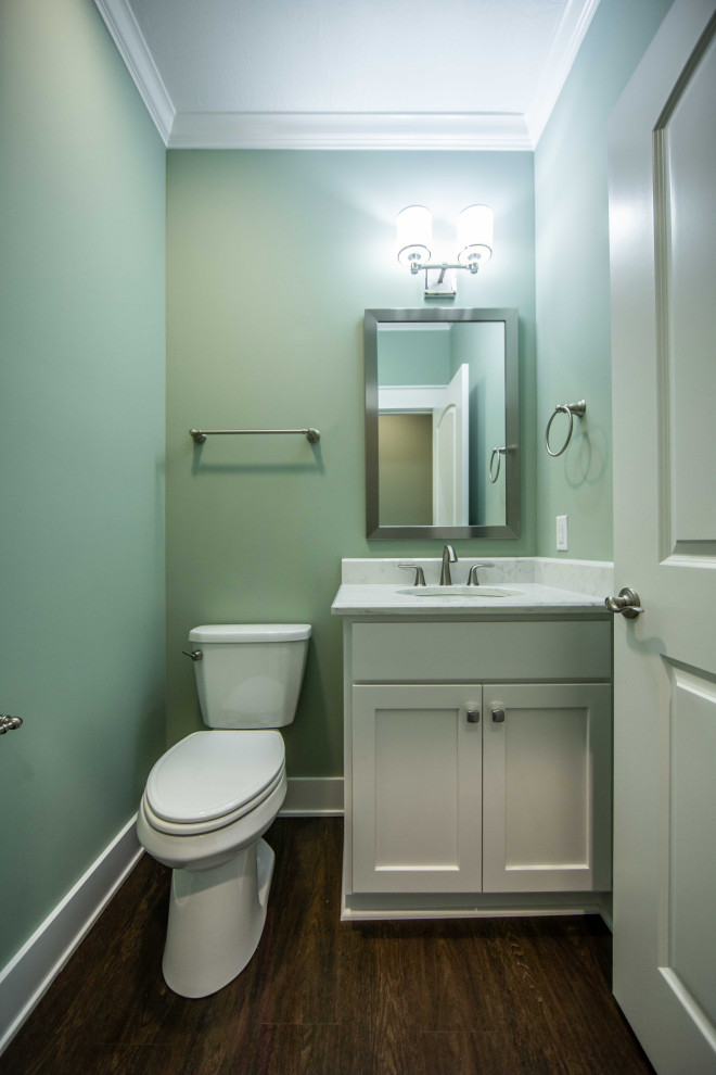 Foto på ett litet vintage vit badrum, med luckor med infälld panel, vita skåp, en toalettstol med separat cisternkåpa, gröna väggar, mellanmörkt trägolv, ett undermonterad handfat, marmorbänkskiva och brunt golv
