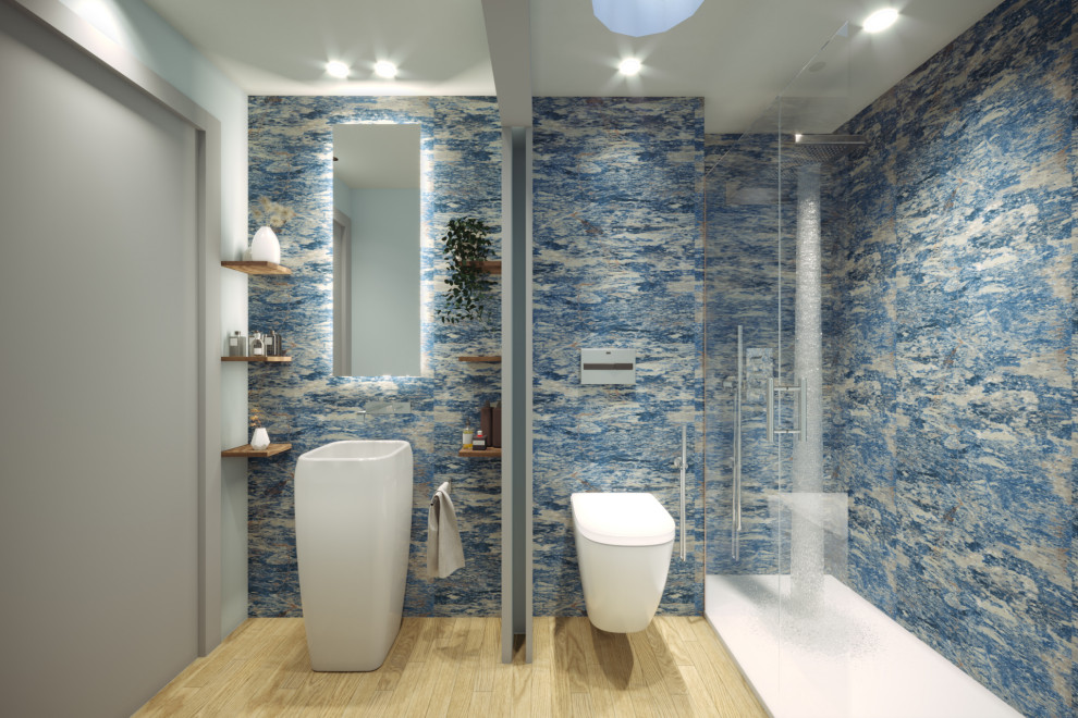 Bild på ett litet funkis toalett, med en toalettstol med hel cisternkåpa, blå kakel, porslinskakel, grå väggar, mellanmörkt trägolv, ett piedestal handfat och brunt golv