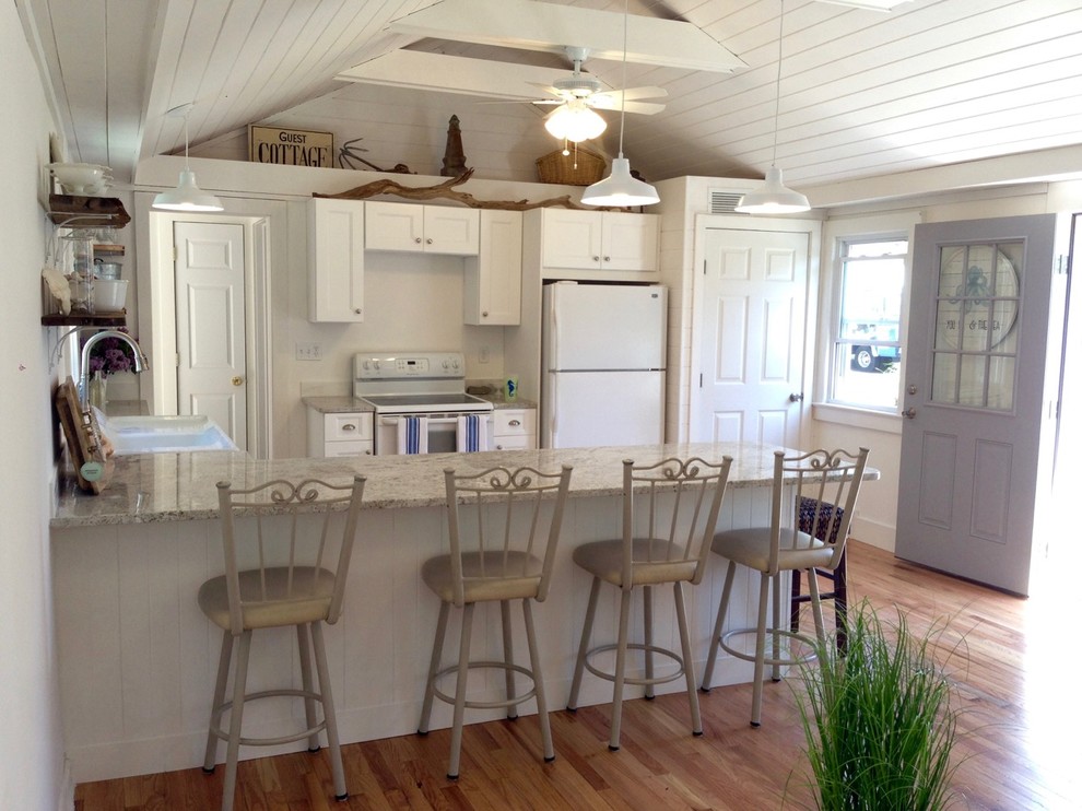 This is an example of a small beach style u-shaped open plan kitchen in New York with a double-bowl sink, shaker cabinets, white cabinets, white appliances, medium hardwood floors and a peninsula.