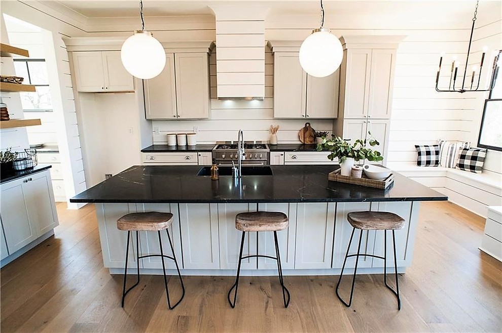 Photo of a mid-sized transitional l-shaped open plan kitchen in Miami with an undermount sink, shaker cabinets, white cabinets, onyx benchtops, white splashback, timber splashback, stainless steel appliances, light hardwood floors, with island, beige floor and black benchtop.