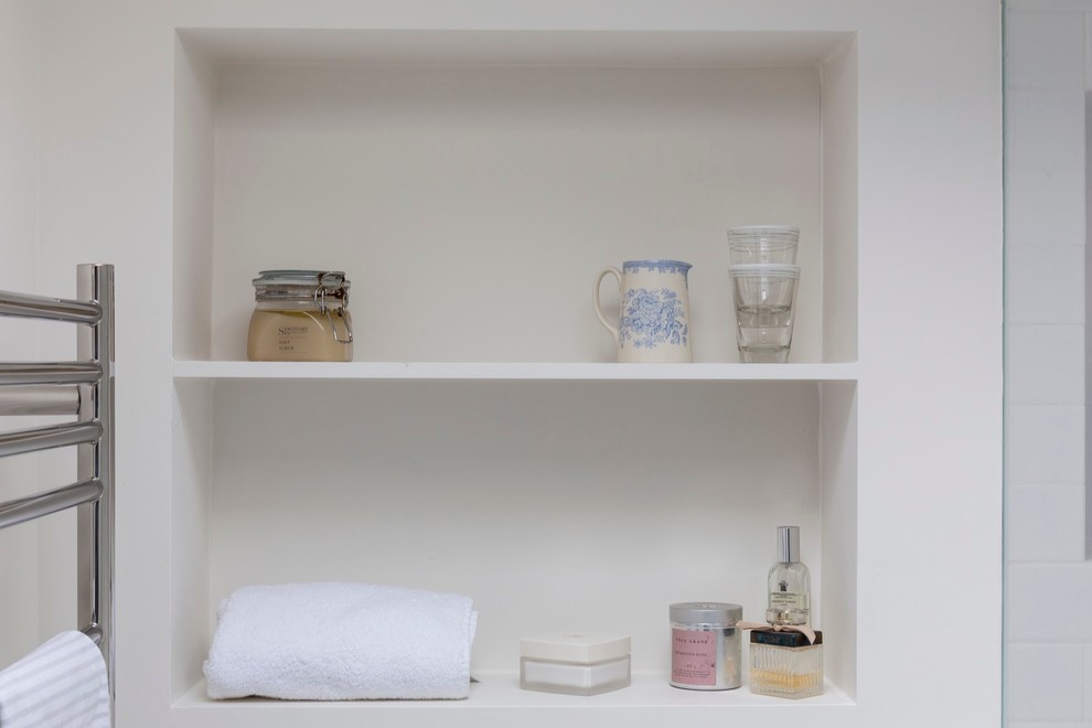 This is an example of a small transitional master bathroom in London with open cabinets, white cabinets, an open shower, a wall-mount toilet, white tile, white walls, ceramic floors and a wall-mount sink.