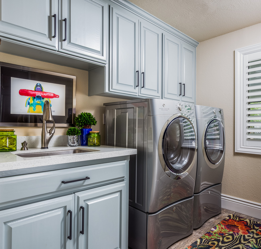 This is an example of a large transitional single-wall dedicated laundry room in San Francisco with a drop-in sink, raised-panel cabinets, blue cabinets, laminate benchtops, beige walls, ceramic floors, a side-by-side washer and dryer and beige floor.