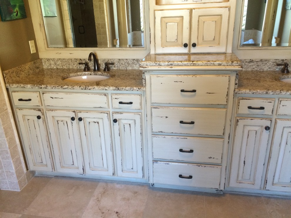 This is an example of a mid-sized country master bathroom in Little Rock with distressed cabinets, ceramic tile, granite benchtops, beige walls, ceramic floors, an undermount sink, raised-panel cabinets and beige tile.