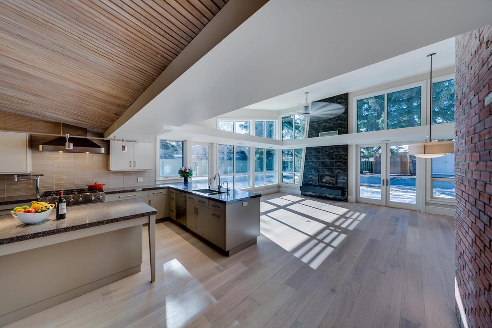 Inspiration for a midcentury u-shaped open plan kitchen in Calgary with a double-bowl sink, flat-panel cabinets, grey cabinets, granite benchtops, grey splashback, ceramic splashback, stainless steel appliances, light hardwood floors and multiple islands.