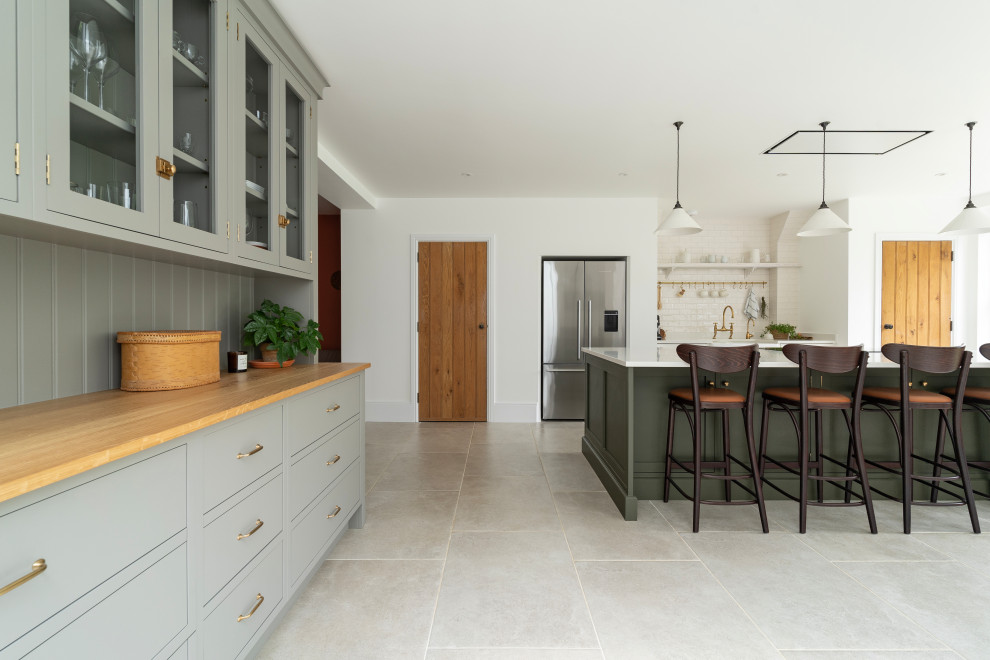 Large traditional grey and white open plan kitchen in Oxfordshire with a belfast sink, shaker cabinets, grey cabinets, quartz worktops, beige splashback, stainless steel appliances, ceramic flooring, an island, grey floors, white worktops and feature lighting.