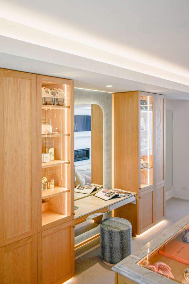 Large contemporary dressing room in Sunshine Coast with glass-front cabinets, light wood cabinets and carpet.