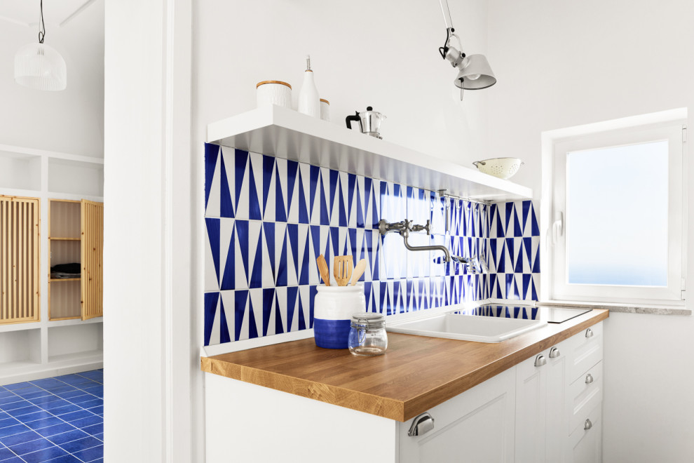 Idéer för små medelhavsstil linjära kök med öppen planlösning, med en enkel diskho, släta luckor, vita skåp, träbänkskiva, blått stänkskydd, stänkskydd i keramik, vita vitvaror, klinkergolv i keramik och blått golv