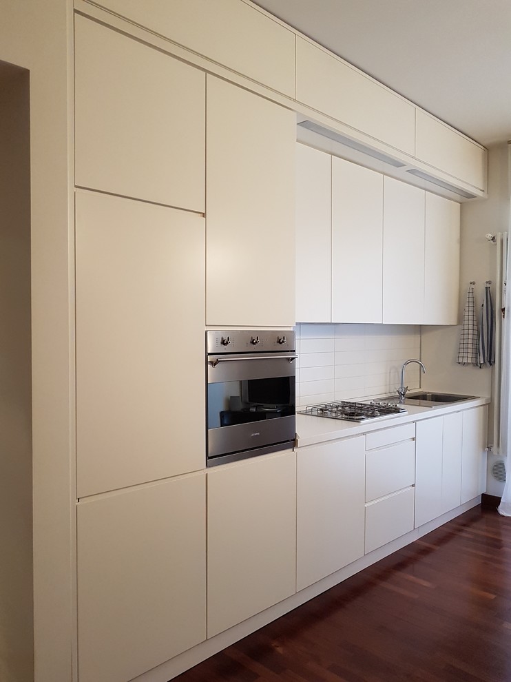 Small contemporary single-wall open plan kitchen in Other with a drop-in sink, flat-panel cabinets, white cabinets, laminate benchtops, white splashback, ceramic splashback, stainless steel appliances, medium hardwood floors and no island.