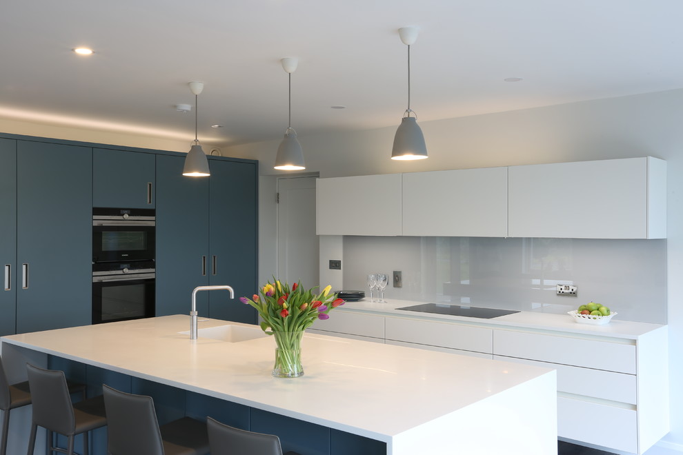 Contemporary kitchen in Dublin with flat-panel cabinets, white cabinets, solid surface benchtops, grey splashback, glass sheet splashback, dark hardwood floors and with island.