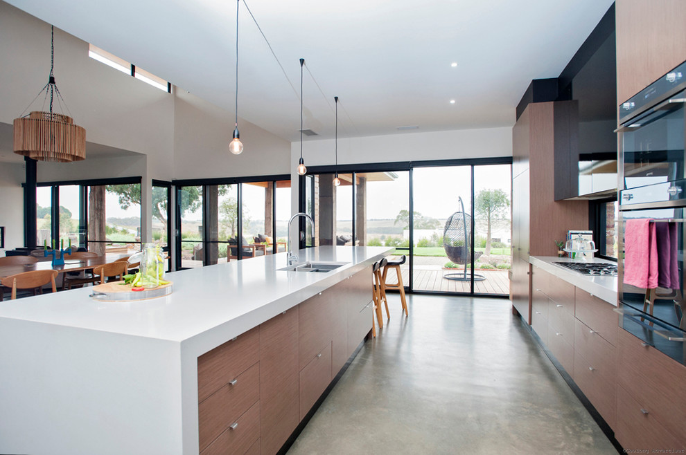 This is an example of a contemporary galley open plan kitchen in Melbourne with with island, flat-panel cabinets, medium wood cabinets, solid surface benchtops, stainless steel appliances and an undermount sink.