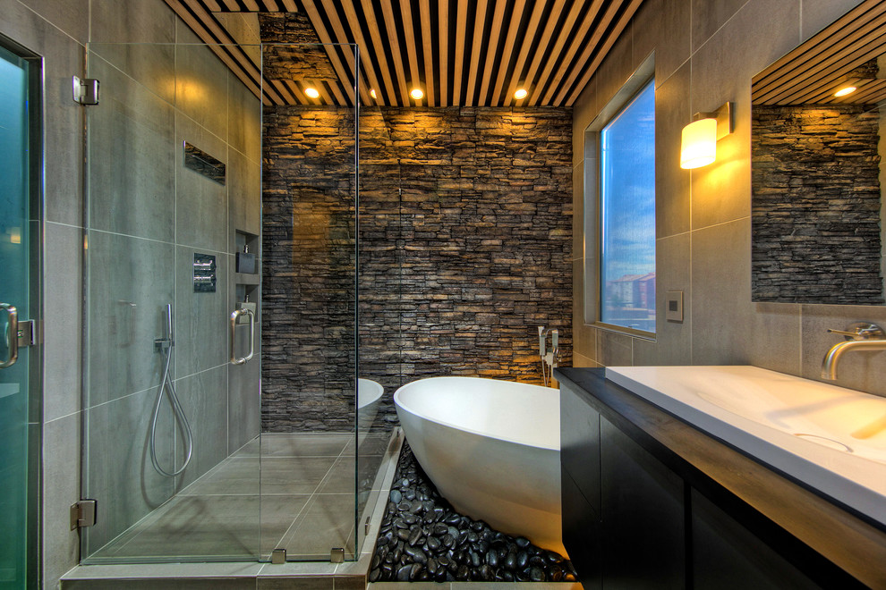 Design ideas for a mid-sized contemporary master bathroom in Phoenix with flat-panel cabinets, dark wood cabinets, a freestanding tub, a corner shower, a one-piece toilet, gray tile, porcelain tile, grey walls, porcelain floors, a wall-mount sink and solid surface benchtops.