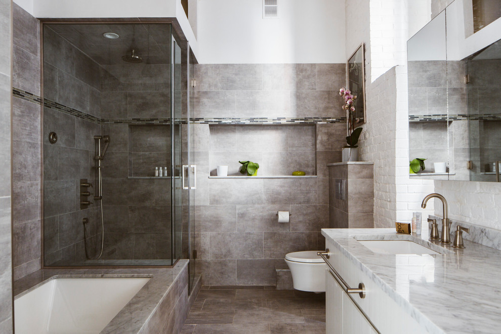 Inspiration for a mid-sized industrial master bathroom in New York with an undermount sink, flat-panel cabinets, white cabinets, granite benchtops, a freestanding tub, an alcove shower, a wall-mount toilet, gray tile, ceramic tile, white walls and ceramic floors.