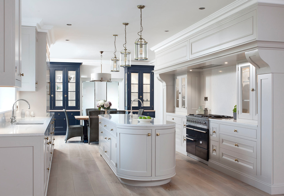 Inspiration for a mid-sized traditional galley eat-in kitchen in Dublin with recessed-panel cabinets, granite benchtops, white splashback, with island, beige floor, grey cabinets, black appliances and light hardwood floors.