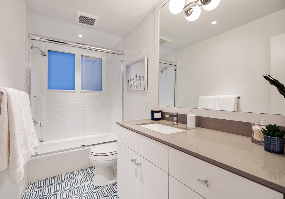 Réalisation d'une petite salle de bain principale marine avec un placard à porte plane, des portes de placard blanches, une baignoire posée, un combiné douche/baignoire, WC séparés, un carrelage blanc, des carreaux de céramique, un mur blanc, un sol en carrelage de porcelaine, un lavabo encastré, un plan de toilette en quartz modifié, un sol bleu, une cabine de douche à porte coulissante, un plan de toilette beige, meuble simple vasque et meuble-lavabo encastré.