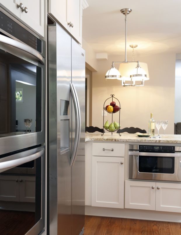 Example of a mid-sized transitional l-shaped dark wood floor eat-in kitchen design in Cedar Rapids with a farmhouse sink, shaker cabinets, white cabinets, granite countertops, white backsplash, subway tile backsplash, stainless steel appliances and an island