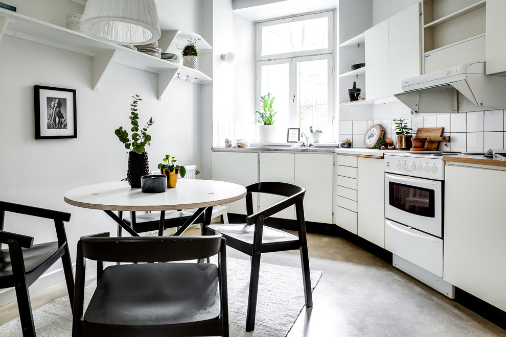 Scandinavian single-wall eat-in kitchen in Stockholm with flat-panel cabinets, white cabinets, white splashback, white appliances, concrete floors, no island and grey floor.