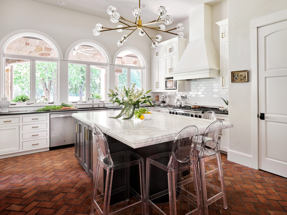 Kitchen - huge traditional u-shaped brick floor kitchen idea in Austin with an undermount sink, shaker cabinets, white cabinets, marble countertops, white backsplash, subway tile backsplash, stainless steel appliances and an island