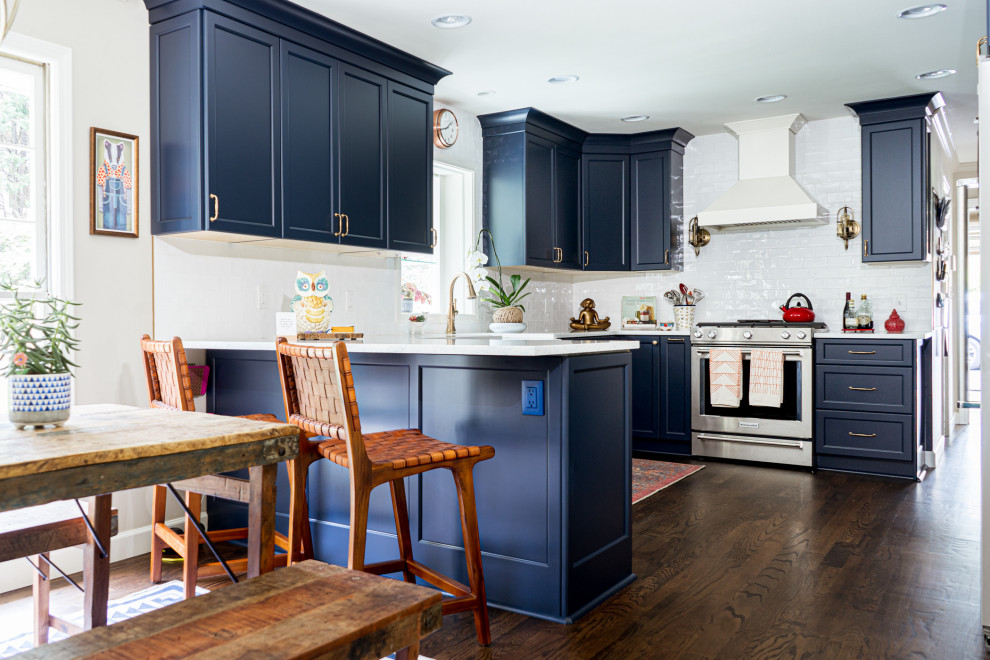 Small eclectic l-shaped kitchen/diner in Atlanta with a belfast sink, shaker cabinets, blue cabinets, engineered stone countertops, blue splashback, ceramic splashback, stainless steel appliances, medium hardwood flooring, a breakfast bar, brown floors and blue worktops.