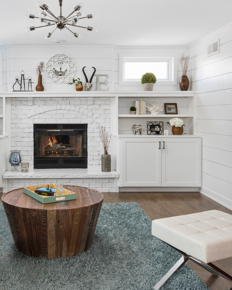 Photo of a mid-sized transitional open concept family room in Chicago with white walls, medium hardwood floors, a standard fireplace, a brick fireplace surround, a wall-mounted tv, grey floor and planked wall panelling.